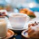 A breakfast table with a cup of coffee, pastries and milk