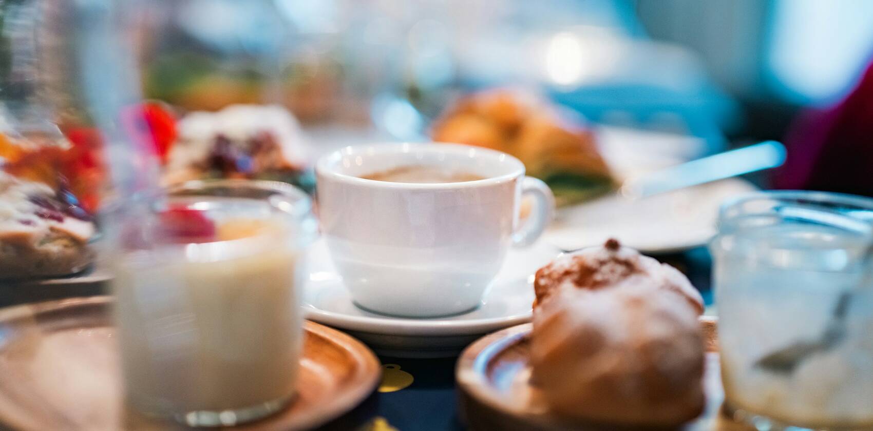 A breakfast table with a cup of coffee, pastries and milk