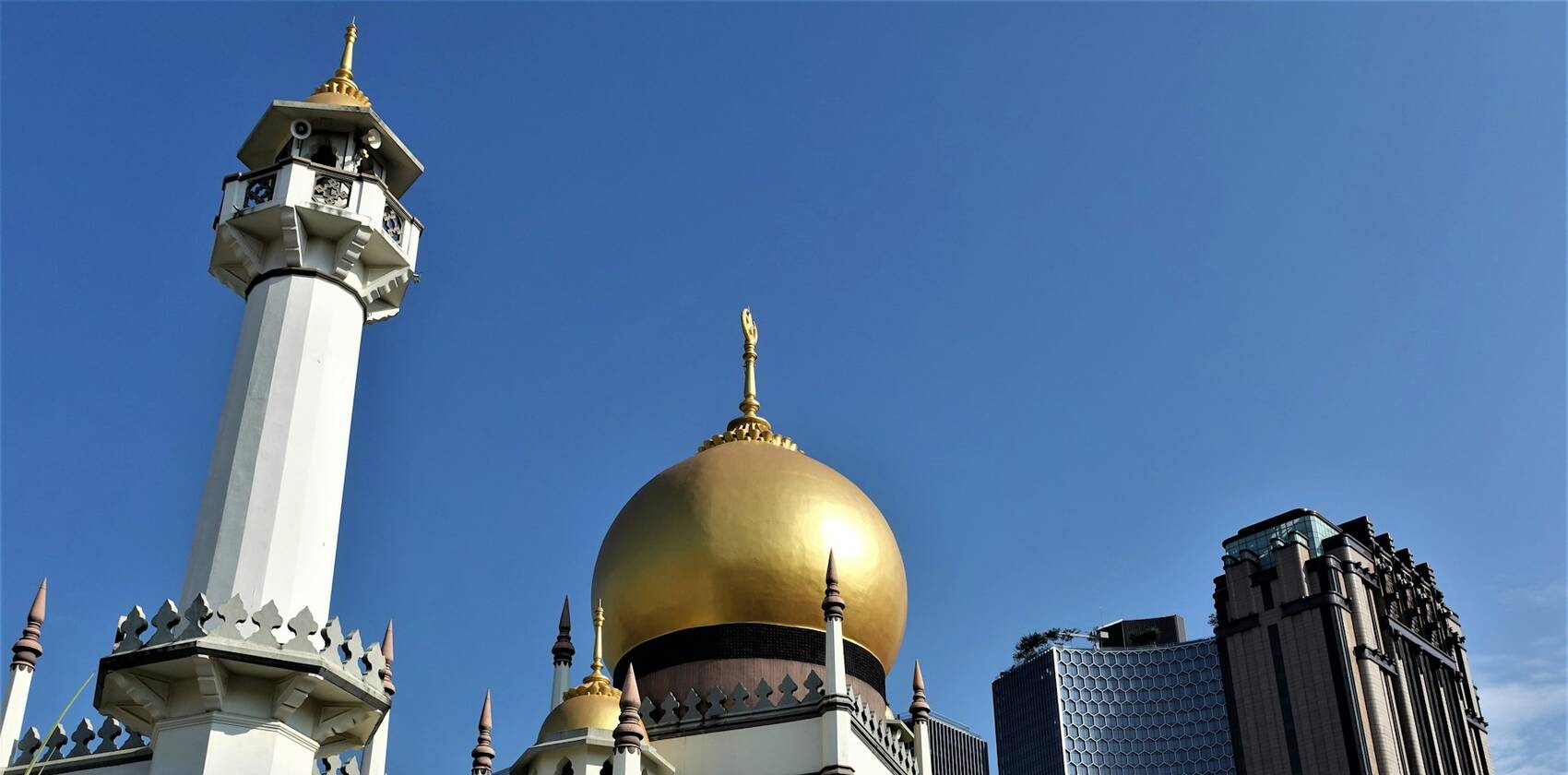 The minaret and golden dome of Sultan Mosque against a blue sky